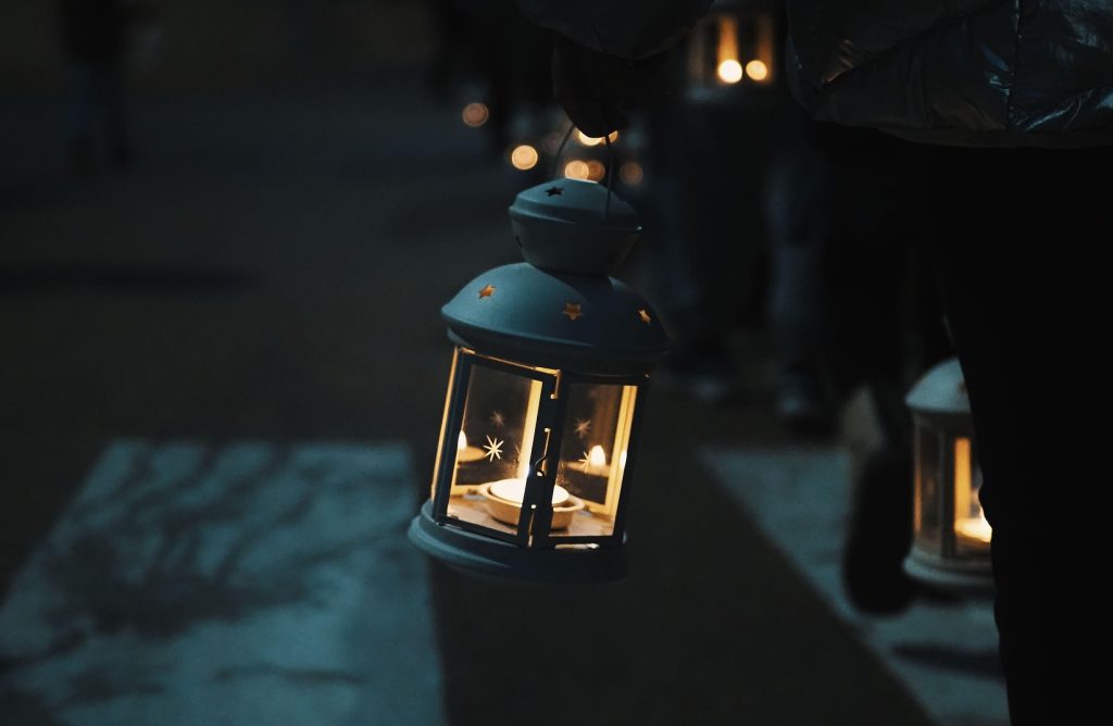 A person holding a white vintage-style lantern with a glowing tea light candle inside, casting a warm light onto the ground during a dark night walk, representing the path forward in Therapy for Fear of Emotional Intimacy.