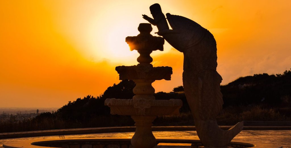 A stone sculpture of a whale-shaped fountain silhouetted against a vivid sunset, symbolizing emotional healing in therapy and renewal after inner storms.