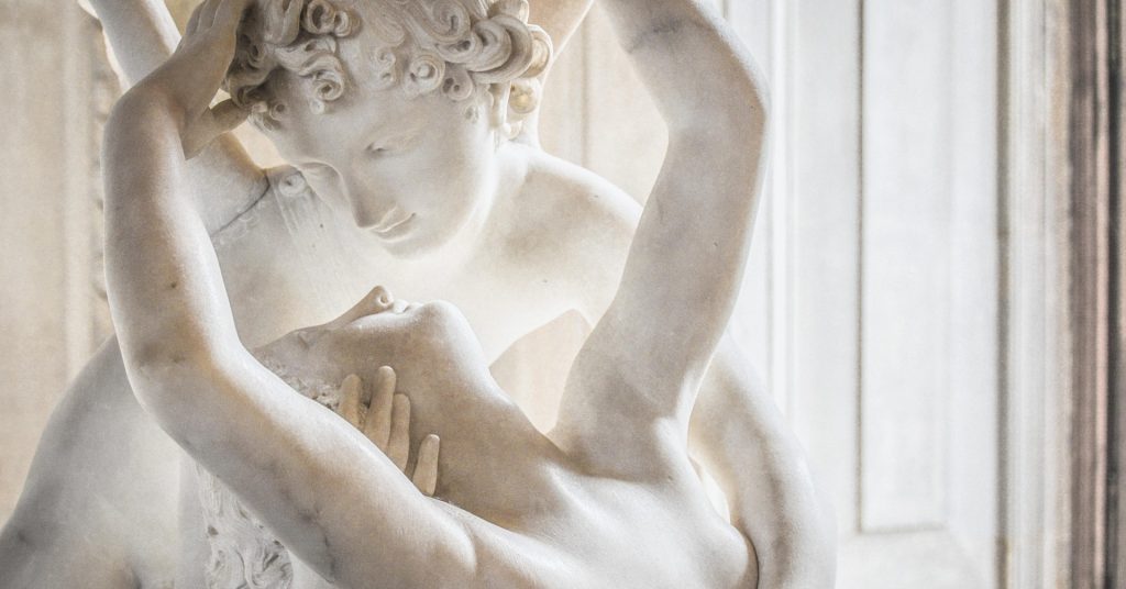 A neoclassical marble sculpture depicting Echo and Narcissus, where Echo leans toward Narcissus in yearning as he gazes into his reflection, symbolizing emotional distance and missed connection.