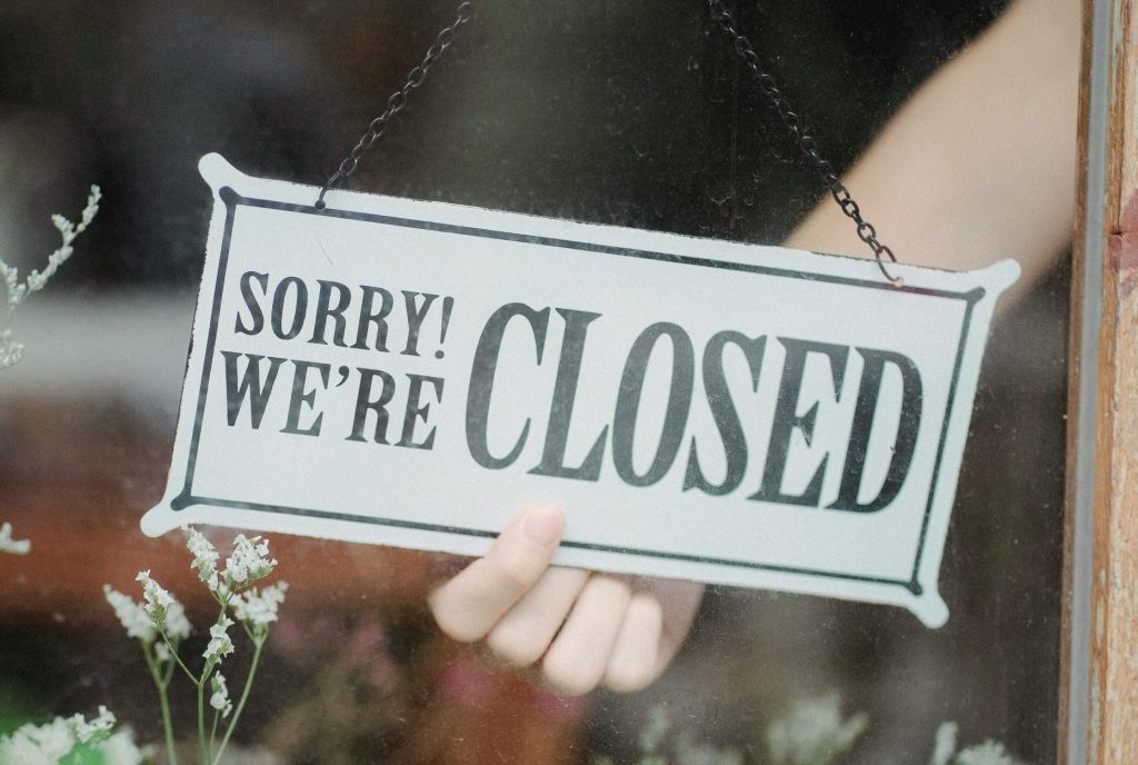 How to apologize effectively represented by A hand hanging a "Sorry! We're Closed" sign on a glass door, illustrating the transactional psychology of apology.
