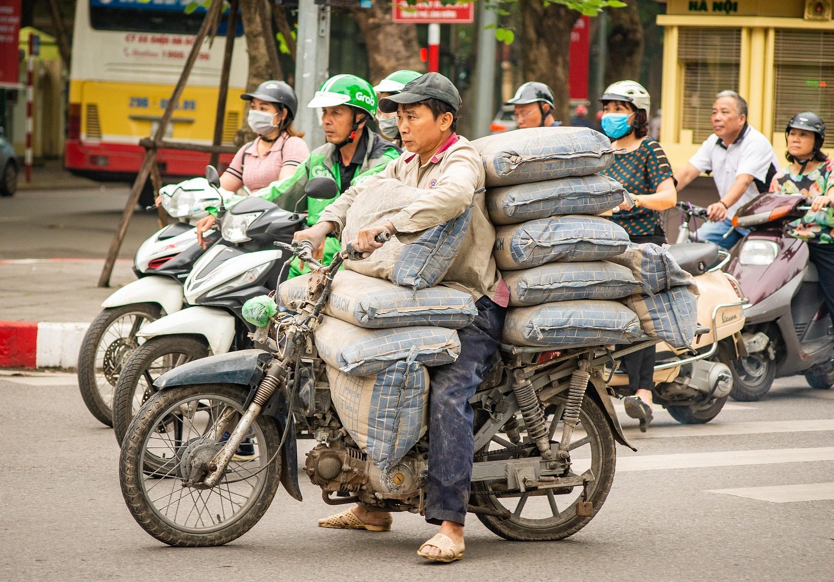 A worker carries heavy sacks on a motorcycle in busy Hanoi traffic. This visualizes the exhaustion that makes us ask why am I so lonely and tired.